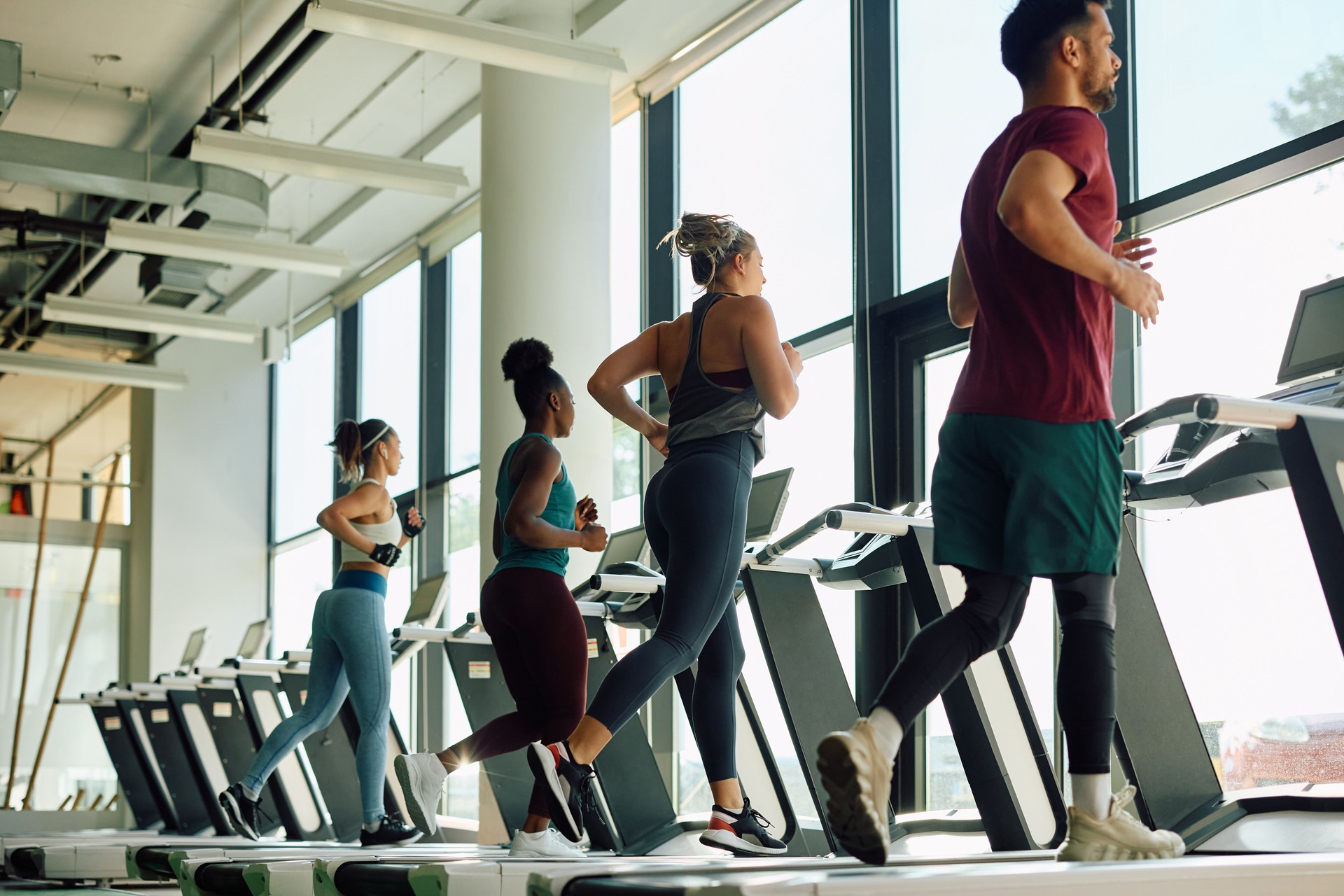 Rear view of athletic people running on treadmill in a gym.